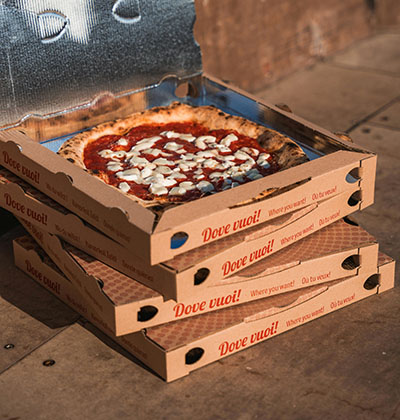 A stack of pizza boxes with the top boa being open, and the pizza showing.